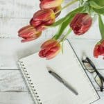 a notepad, pen, glasses and tulips on a white wooden table