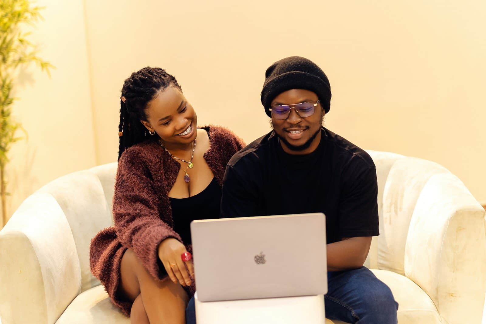 A man and a woman sitting on a couch with a laptop